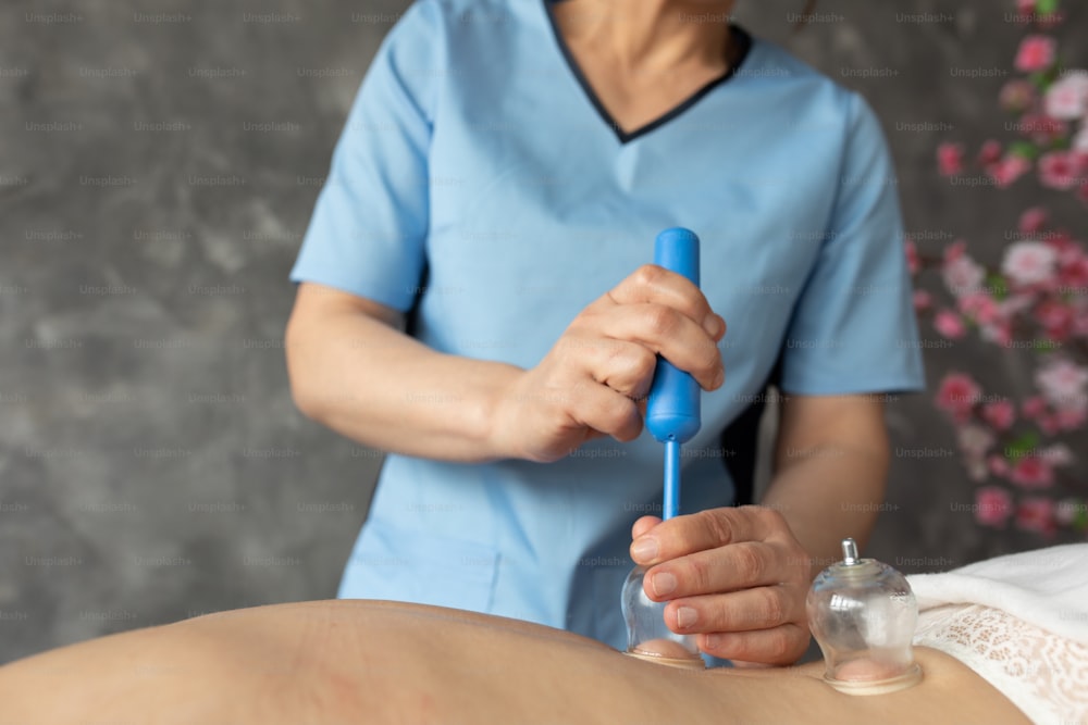 Unrecognizable cropped female physiotherapist doing vacuum cupping massage for patient in spa center. Removing cellulite and friable folds. Perfect skin, healthy back muscles. Medical cupping therapy