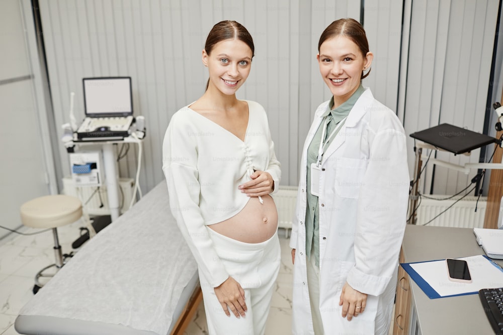 의료 클리닉에서 여의사와 함께 포즈를 취하는 임신한 젊은 여성의 허리 위로 초상화, 복사 공간