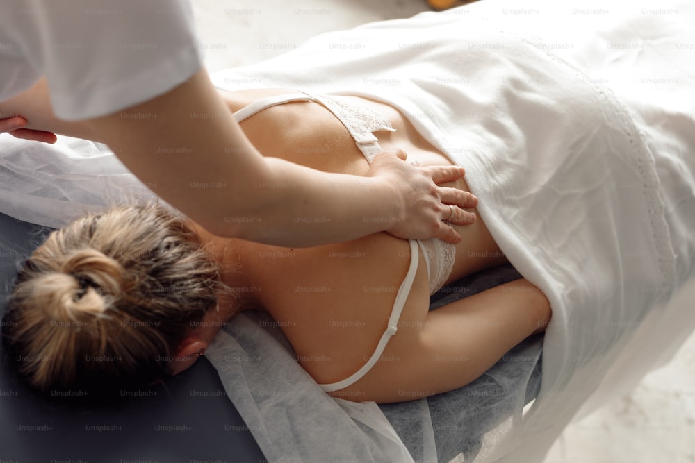 Osteopath in medical cabinet check up spine of woman lying down on hospital couch under white coverlet closeup. Professional specialist appointment and examination. Healthcare and disease treatment.