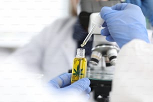 Close-up of persons hand drip blob of cannabinoid oil. Medical worker going to investigate sample under microscope. Modern laboratory and chemistry concept
