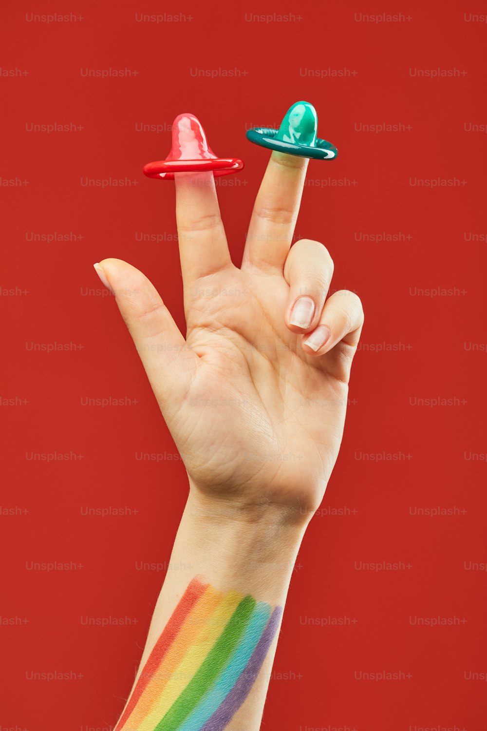 콘돔과 LGBTQ 깃발을 든 생생한 손 샷 빨간 배경에 안전한 섹스 및 보호 개념