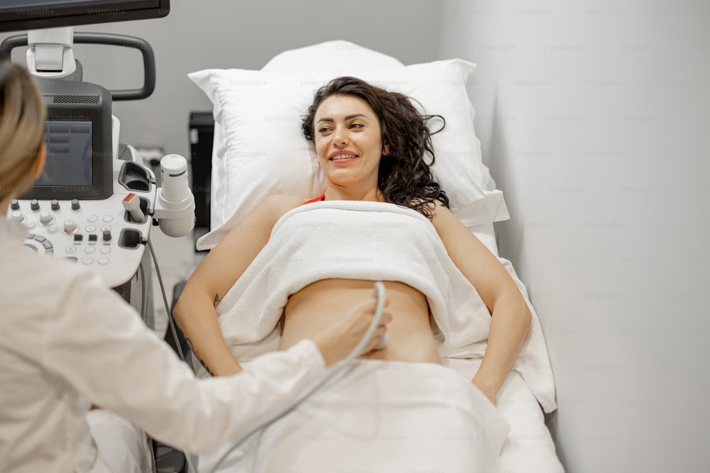 Glückliche erwachsene Frau bei einer Ultraschalluntersuchung der Bauchhöhle in einer modernen Arztpraxis. Konzept der Frauengesundheit und Untersuchung während der Schwangerschaft