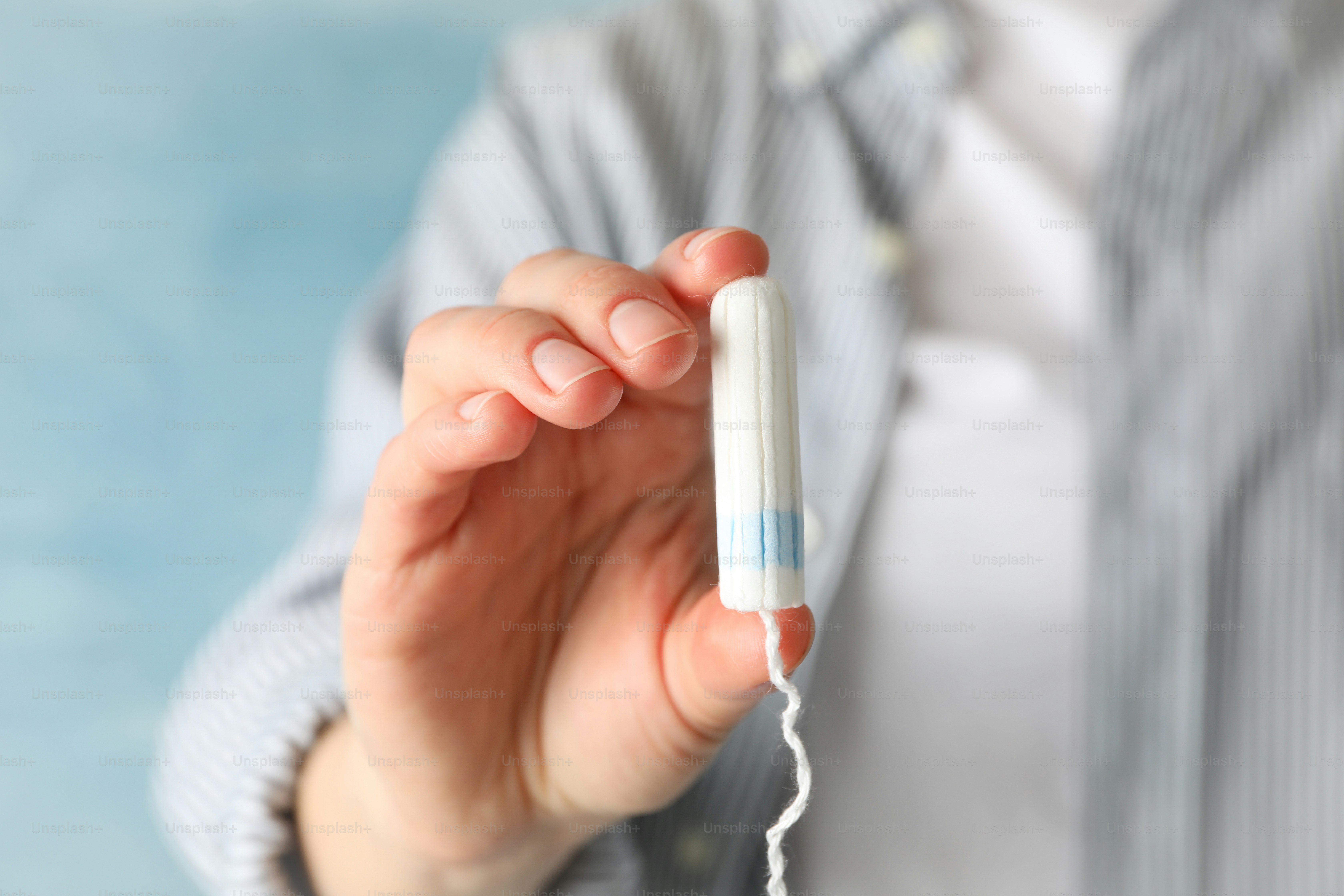 Woman holding tampon against blue background, close up