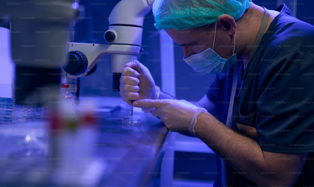 Genetic laboratory worker examining fluid under microscope, studying fertility innovation way, biotechnologies