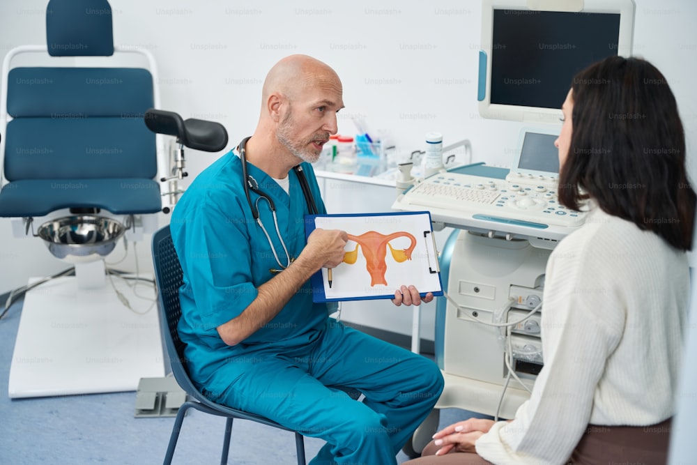 Un trabajador médico concentrado le dice recomendaciones a la paciente mientras tiene en sus manos un diagrama de la estructura del cuerpo femenino