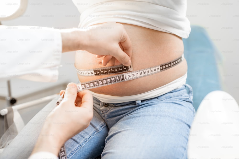 Medico che misura la pancia della donna incinta con un nastro durante una visita medica, vista ritagliata senza viso focalizzata sull'addome