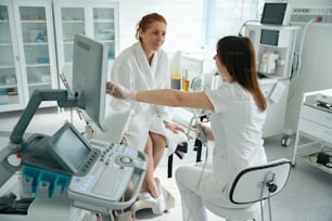 Female patient sitting in robe on the gynecological chair and listening to results of transvaginal ultrasound examination from her doctor at clinic