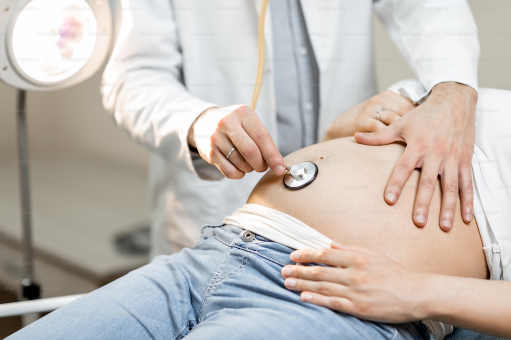 Doctor listening to a pregnant woman's belly with a stethoscope during a medical examination, close-up view