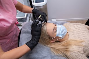 Woman getting injection into scalp, mesotherapy, hair loss therapy. Doctors wearing gloves in salon making medical manipulations to patient.