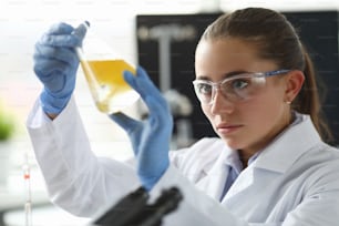 Chemist girl looks at flask with yellow liquid. Experiments and research pharmacist. Laboratory studies virus in under microscope. Incubation period infectious diseases. Test tubes for analysis