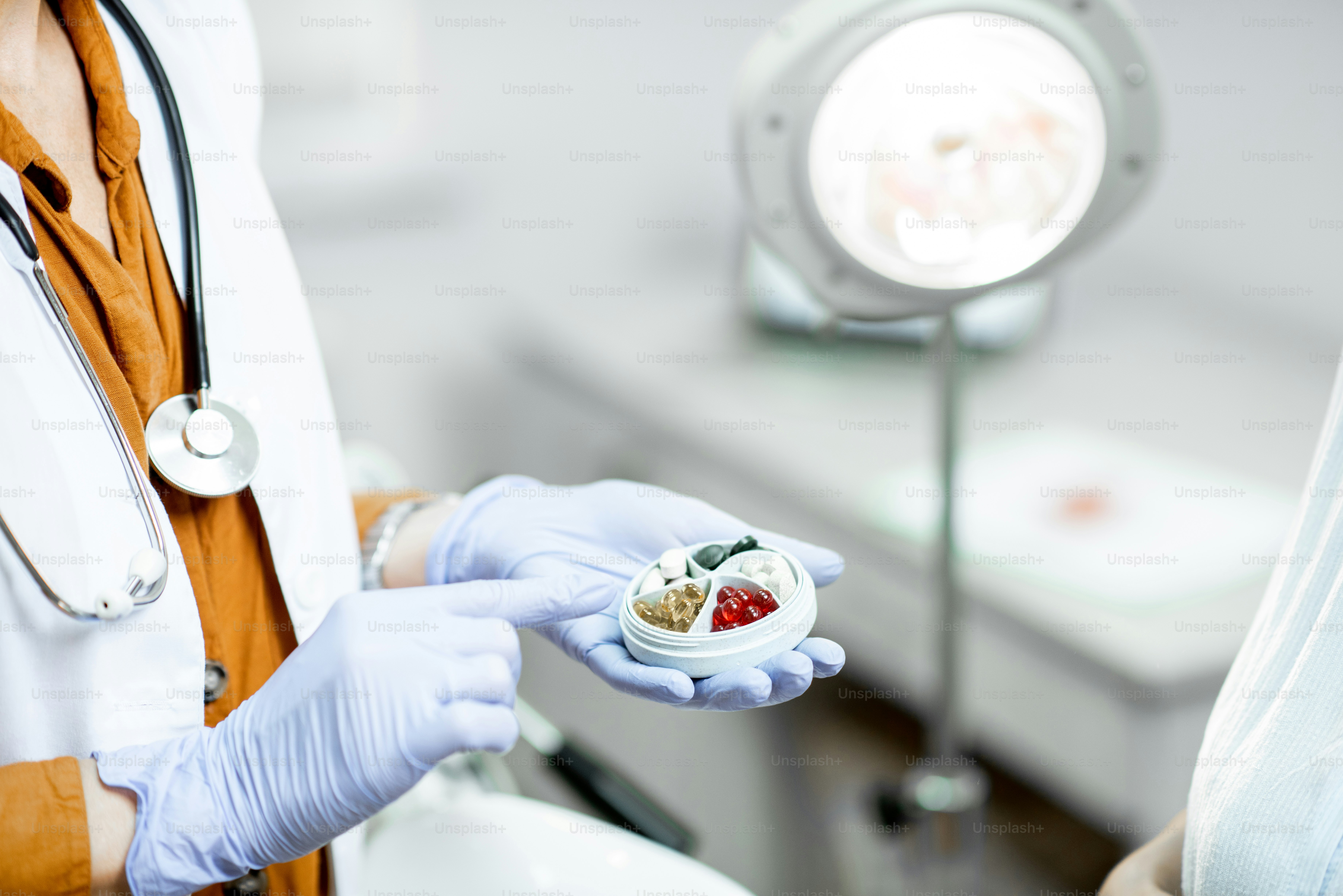 Médico sosteniendo pastillero con un poco de medicina en el consultorio ginecológico, vista de cerca de las manos y las píldoras