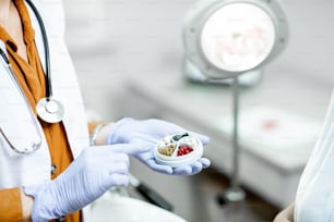 Médico sosteniendo pastillero con un poco de medicina en el consultorio ginecológico, vista de cerca de las manos y las píldoras
