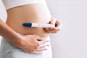 Young woman holding pregnancy test in hands and hugging her belly. Concept of pregnanc, gynecology, medical test, women health.