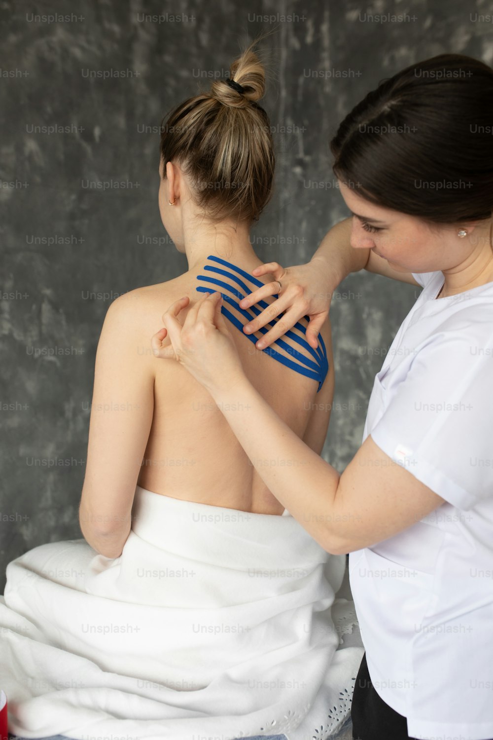Vertical doctor, physiotherapist applying kinesio tapes on back muscles as kinesiology therapy treatment. Female patient injured, backache. Athlete sport traumatic rehabilitation. Scoliosis correction