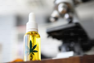 Konzentriere Dich auf eine Glasflasche mit Cannabinoidöl und grünem Ganja-Symbol darauf. Laborinnenraum mit Mikroskop auf verschwommenem Hintergrund. Medizin und medizinisches Marihuana-Konzept
