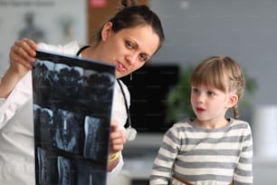 Mulher médica mostra paciente criança um raio-x na clínica. Uso do diagnóstico radiológico de doenças do sistema esquelético no conceito da prática pediátrica.