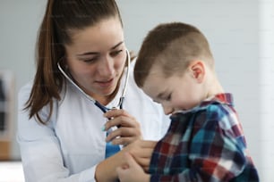 Portrait of cheerful little boy on examination by pediatrician. Doctor listening to breathing or action heart of ill patient with stethoscope. Healthcare and medicine concept