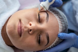 mulher jovem recebendo procedimento profissional de cavitação ultrassonográfica da pele facial como esfoliação, rejuvenescimento e hidratação do cosmetologista