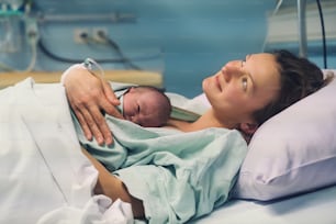 お母さんと新生児。産院での出産。出産後、生まれたばかりの赤ちゃんを抱きしめる若いお母さん。出産する女性。分娩後の赤ちゃんの人生の最初の瞬間。