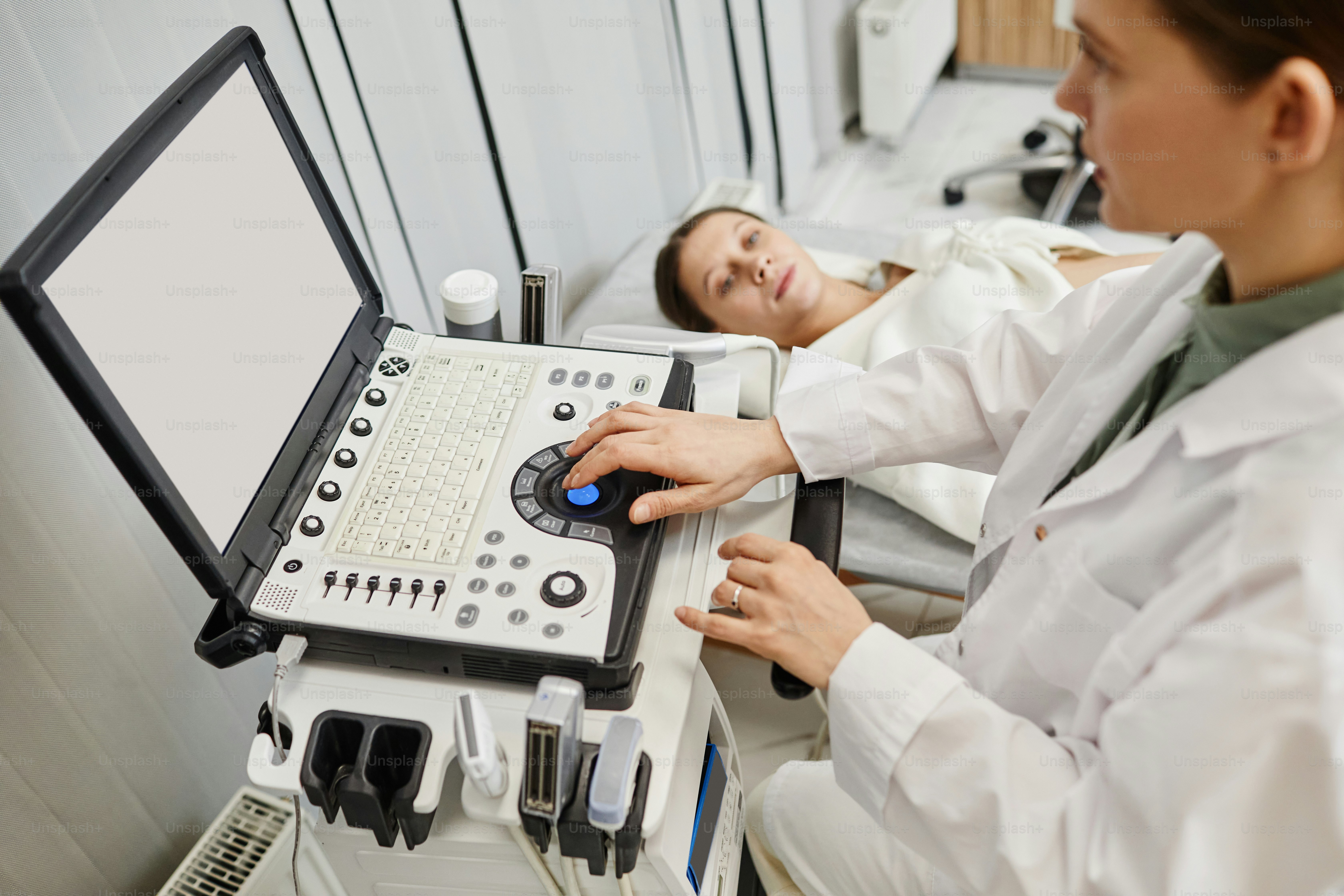 Close up of female doctor using ultrasound machine while examining pregnant young woman in clinic