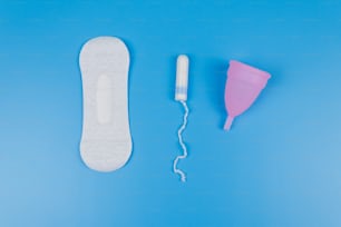 Toalla sanitaria, tampones y copa menstrual sobre fondo azul. Vista superior. Concepto de días críticos, menstruación, higiene femenina