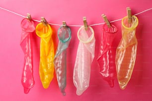 Multicolored condoms hanging on the rope on pink background