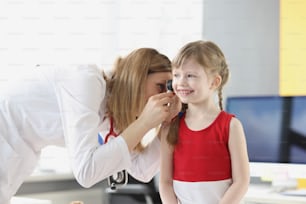 Woman pediatrician examining ear of little girl with otoscope at clinic. Diagnostics and treatment of hearing loss in children concept