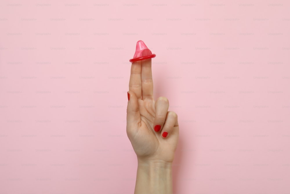 Female hand with condom on pink background
