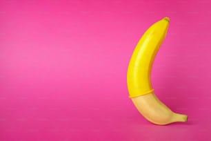 Banana con preservativo giallo su sfondo rosa