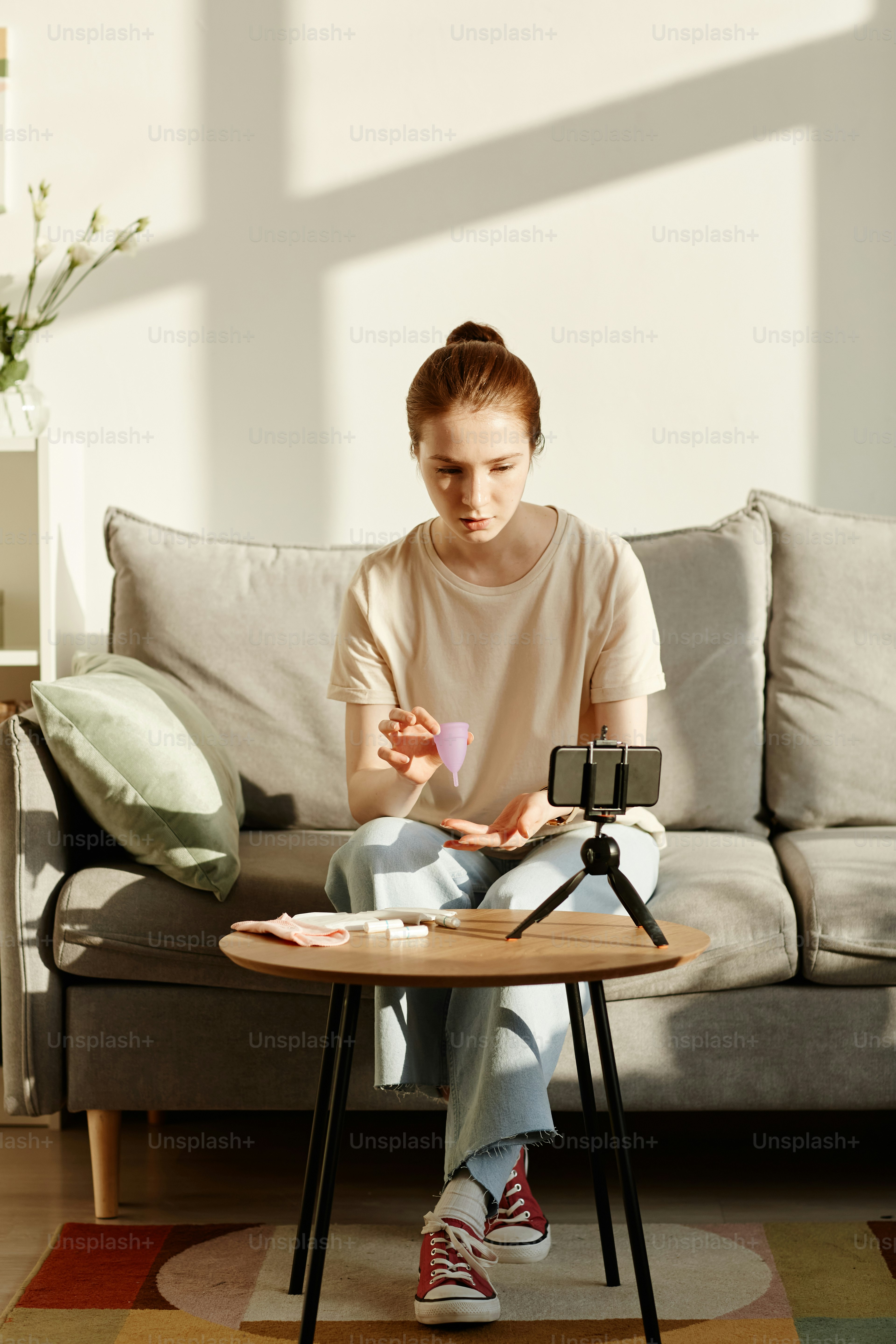 Minimal portrait of Caucasian young woman holding menstrual cup to camera and filming educational video on female hygiene products, copy space