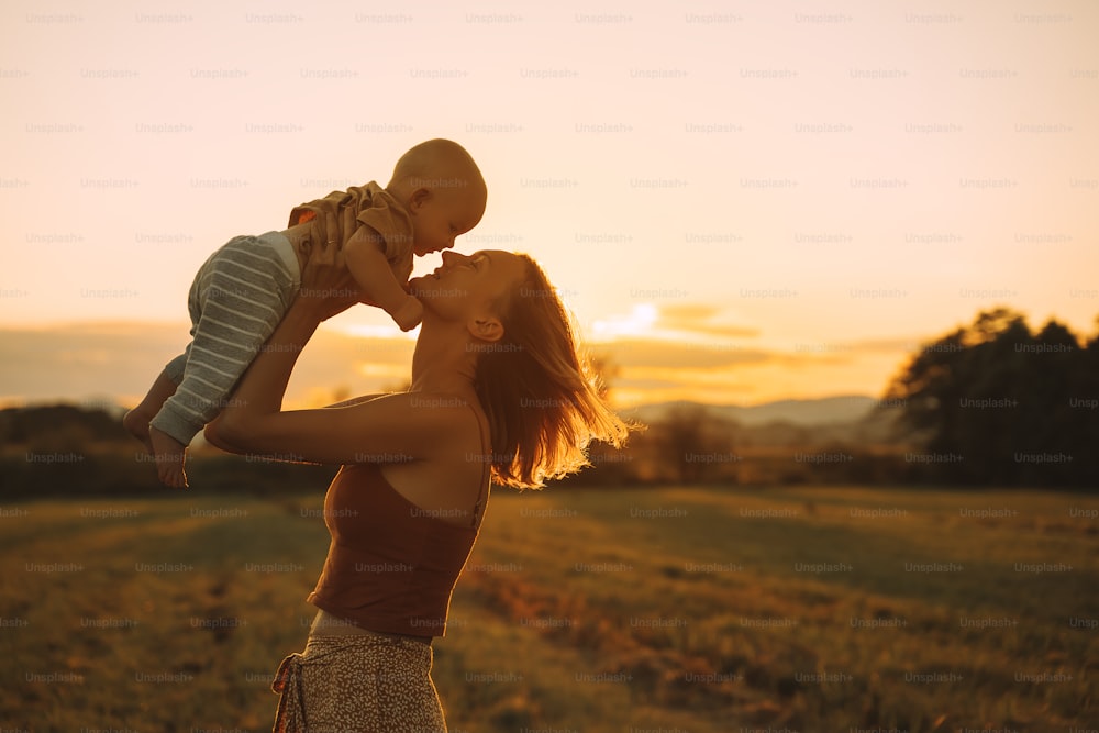 해질녘 사랑하는 엄마와 아기. 자연 배경에 아름 다운 여자와 작은 아이. 타고난 모성의 개념. 여름 야외에서 행복하고 건강한 가족. 긍정적인 인간의 감정과 느낌.