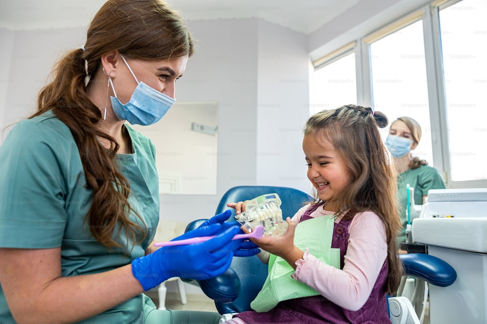 Zahnarzt zeigt Kinderpatienten, wie man die Zahnbürste an Miniaturkiefern in der Klinik verwendet. Gesundheitswesen