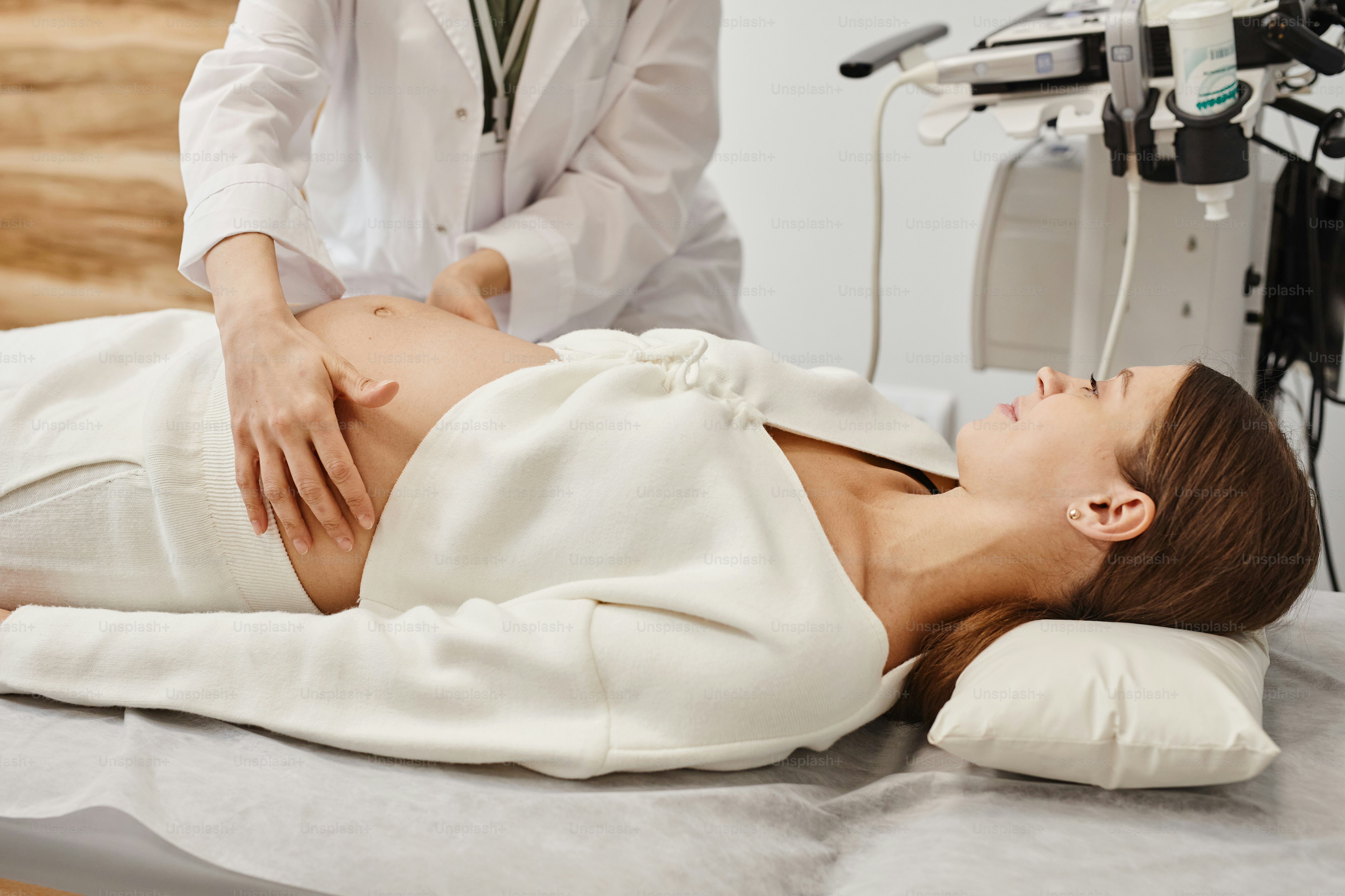 Ritratto di vista laterale di giovane donna incinta che si prepara per l'ecografia in clinica medica con il medico che esamina la pancia