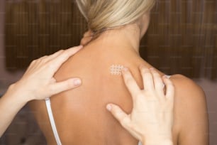 Kinesiotaping, kinesiology cross tape - application for back pain. Woman gets a kinesio cross tape in her neck for pain relief in cervical syndrome. Close-up photo