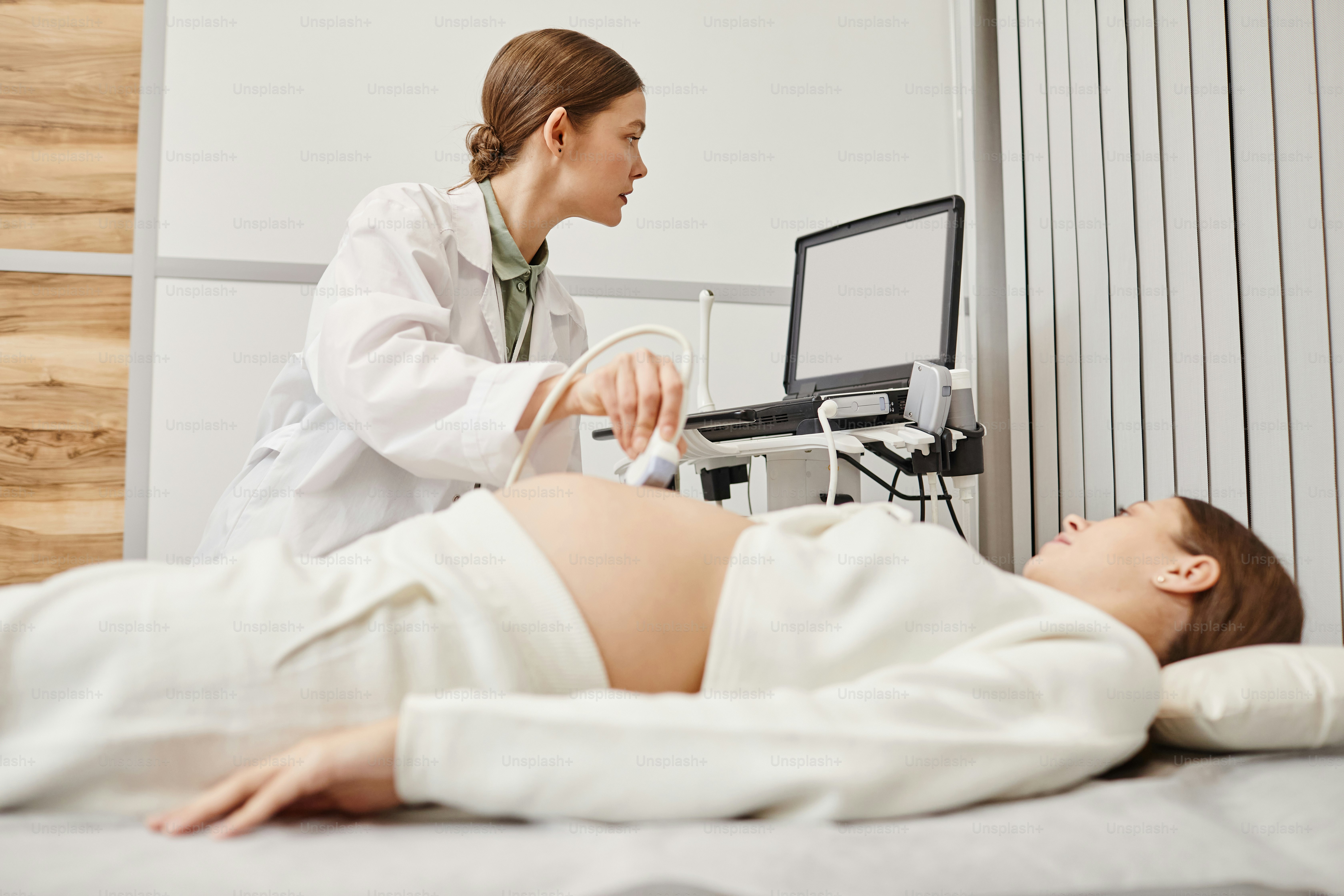 Ritratto di medico femminile che esegue l'esame ecografico su una giovane donna incinta in una clinica medica moderna