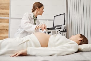 Portrait of female doctor performing ultrasound exam on pregnant young woman in modern medical clinic