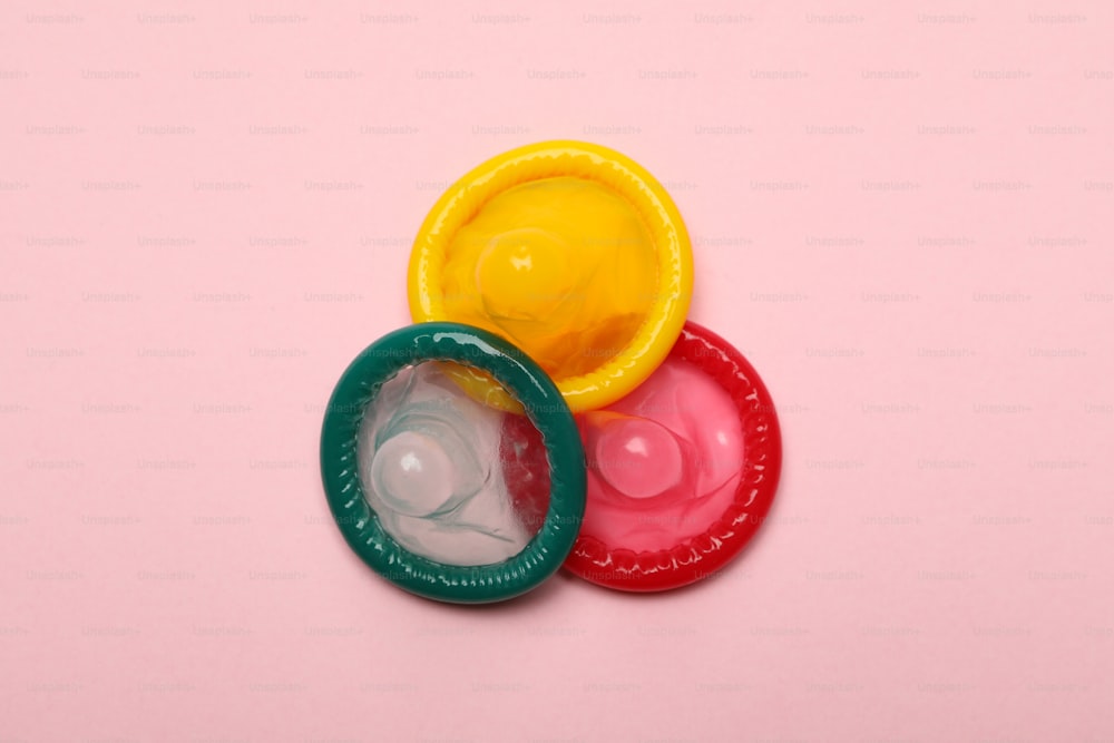 Multicolored condoms on pink background, close up