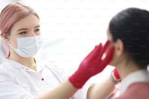 Woman make-up artist in protective mask makes procedure to client in beauty salon. Beauty salon services concept