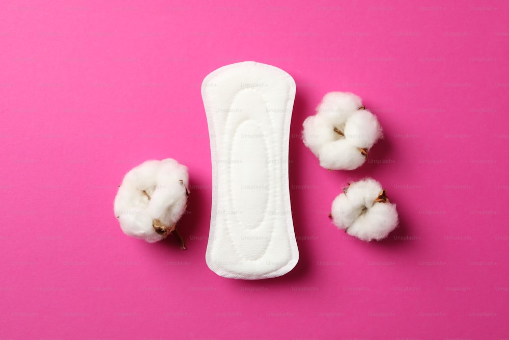 Sanitary pad and cotton on pink background, top view