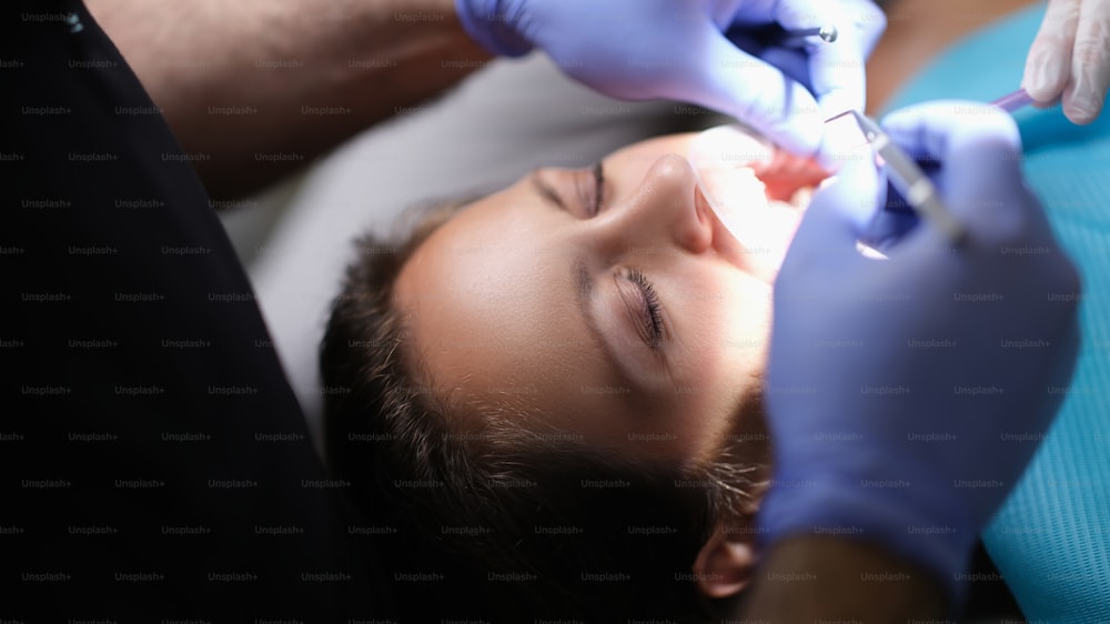 Dentist examines patient teeth at dentist and dental instrument. Doctor examines oral cavity of female patient