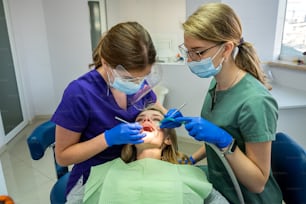 Bonita paciente femenina sentada en el sillón mientras el médico con un asistente examina sus dientes. Concepto de estomatología