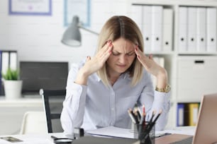 Una mujer cansada se lleva los dedos a las sienes en la mesa de trabajo. Concepto de jornada laboral irregular