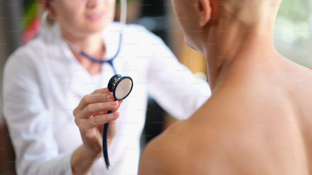 Doctor listens to heart and lungs of young athlete man closeup with stethoscope. Lung disease cough and bronchitis