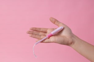 Nahaufnahme auf einem rosa Hintergrund einer Hand, die einen Tampon in einem rosa Applikator hält