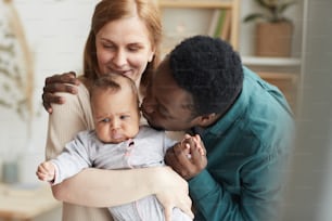 Waist up portrait of loving interracial family at home, focus on African-American man kissing cute mixed race baby