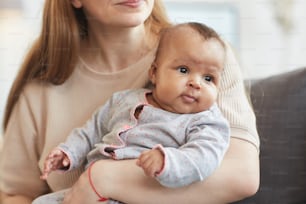 귀여운 혼혈 아기가 돌보는 백인 어머니의 손에 앉아서 시선을 돌리고 있는 초상화, 복사 공간