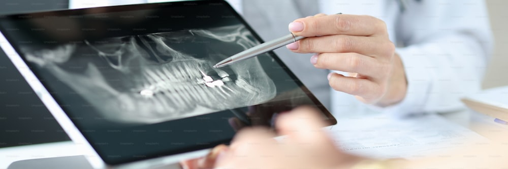 Dentist shows an X-ray of jaw to patient on tablet. Dentist services concept