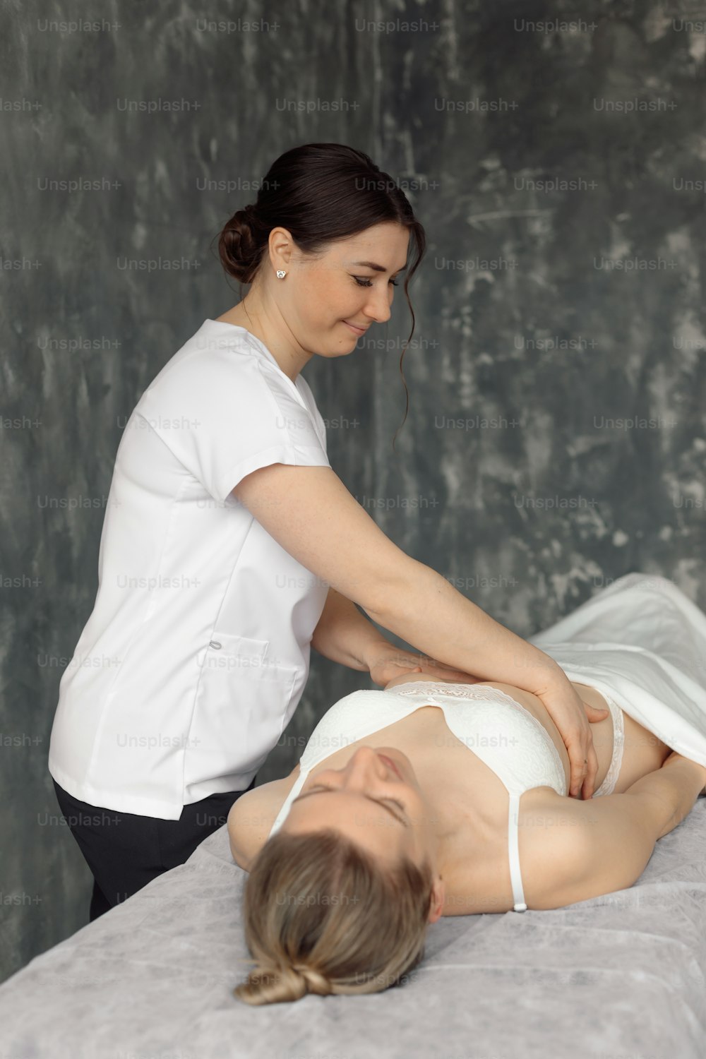 흰 속옷 차림으로 병원 소파에 누워 있는 여성의 갈비뼈를 검진하는 의료 캐비닛의 정골 의사. 전문 전문의 임명 및 검사. 건강 관리 및 질병 치료 개념.