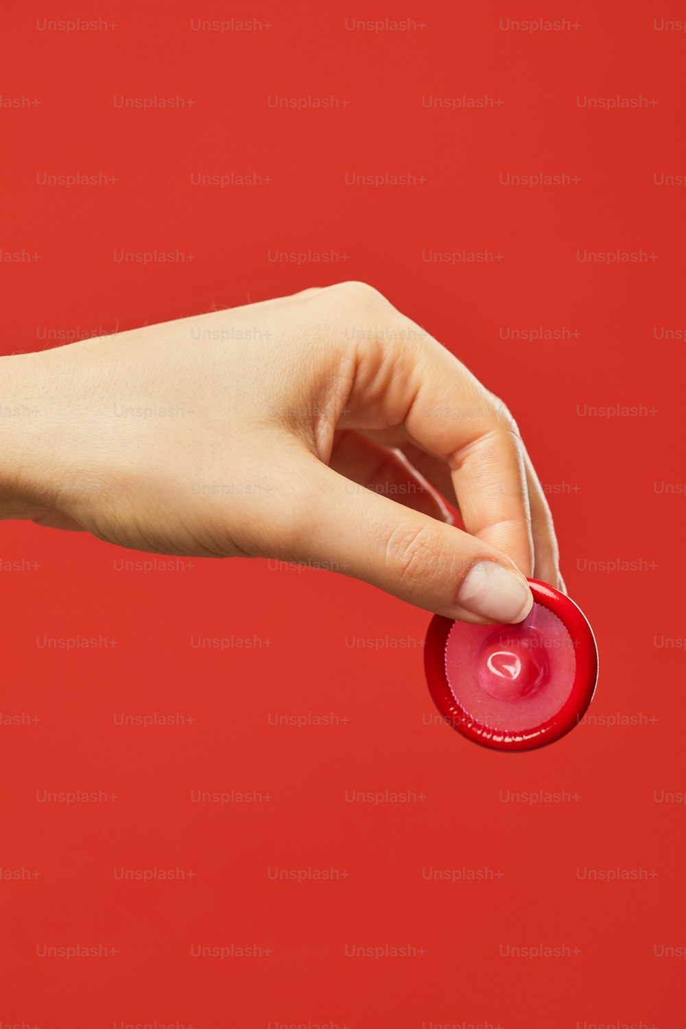 빨간 배경에 콘돔을 들고 있는 여성의 손의 생생한 근접 촬영 안전한 섹스와 보호 개념