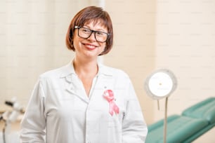 Porträt einer leitenden Gynäkologin mit Hilfsband auf dem Arztkittel im Büro stehend